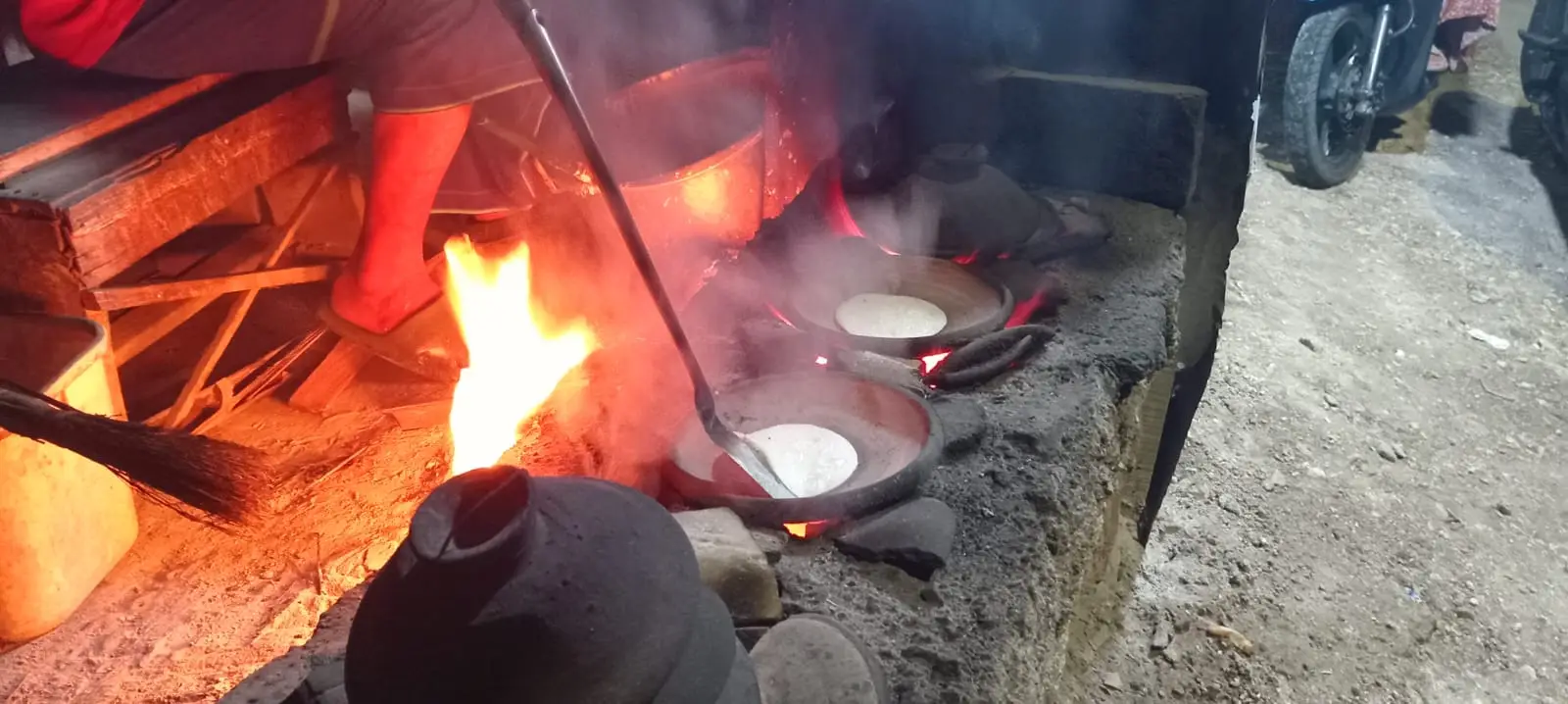 Adonan serabi sedang dimasak di atas tungku dengan api menyala-nyala.