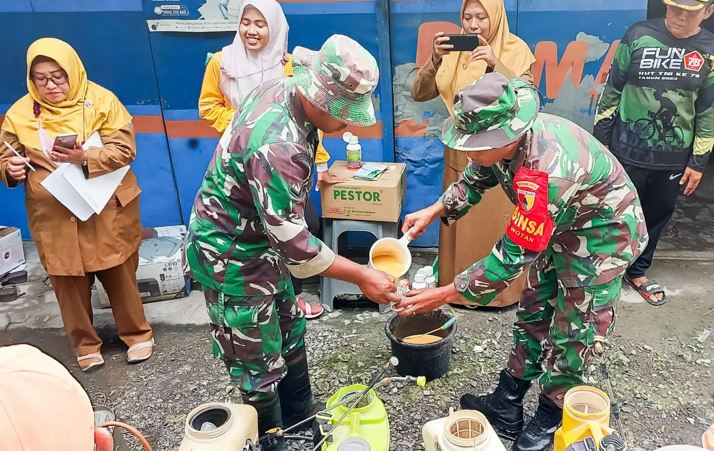Dua orang Babinsa sedang menuang campuran pestisida ke gelas plastik