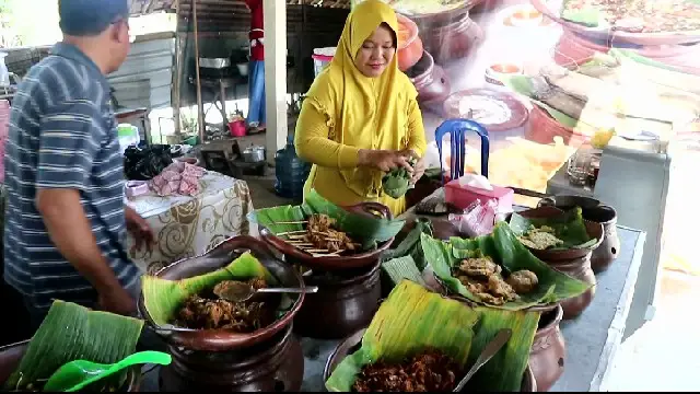 Penjual makanan sedang mengambilkan makanan untuk pelanggan dari berbagai menu yang tersedia di meja.